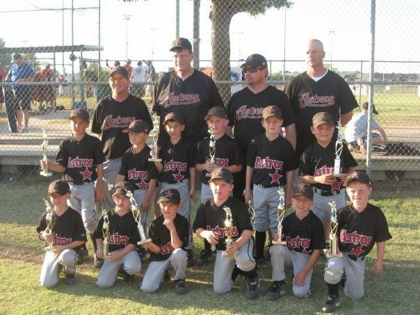 Youth baseball team posing with trophies on a field, wearing black jerseys and caps.