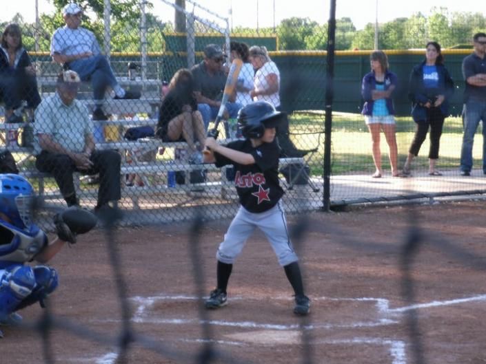 Young baseball player at bat in a youth softball game, with catcher and spectators behind the fence