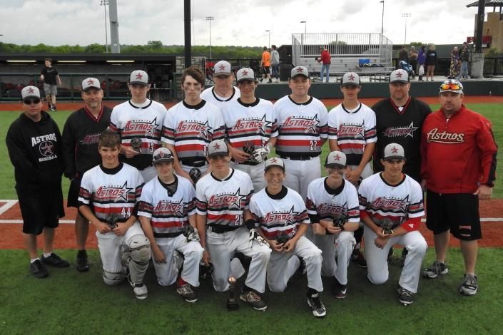 Youth baseball team posing in white and red uniforms on a field with coaches standing behind them
