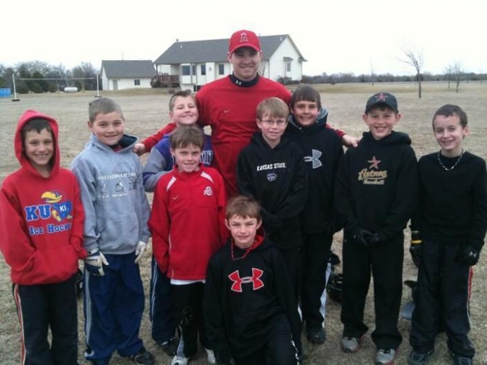 Group of children and two adults posing outdoors on a sports field, most wearing hoodies and jackets.