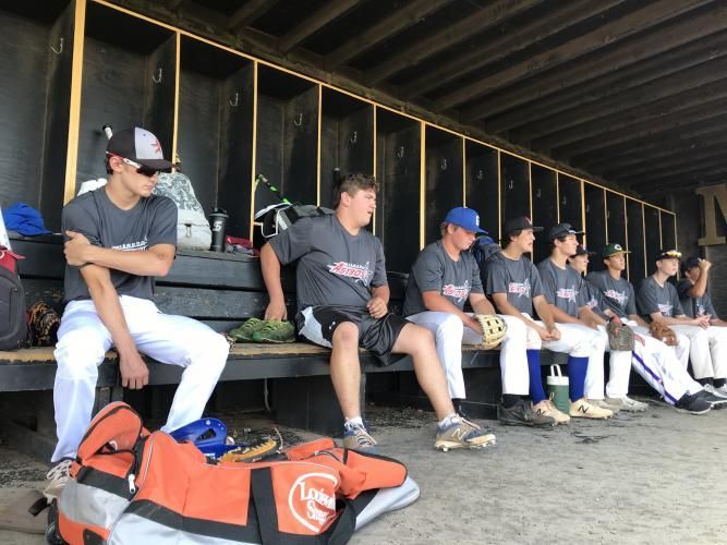 Baseball players in gray uniforms sit on a dugout bench, waiting during a game.