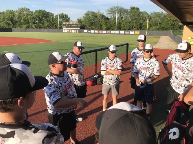 Youth baseball team huddles with a coach on the field before a game, wearing matching uniforms.