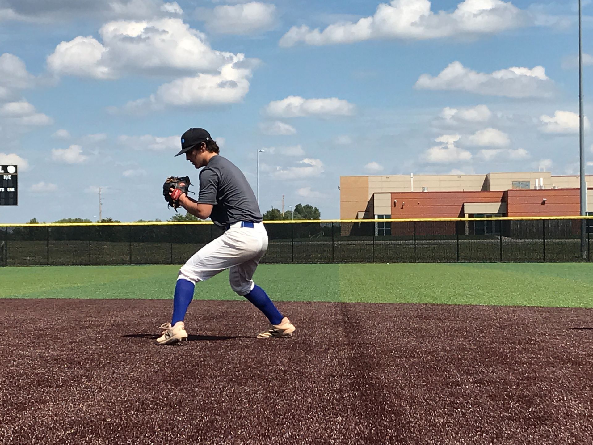 Baseball pitcher in gray uniform and blue socks on a mound, mid-windup under a cloudy sky.