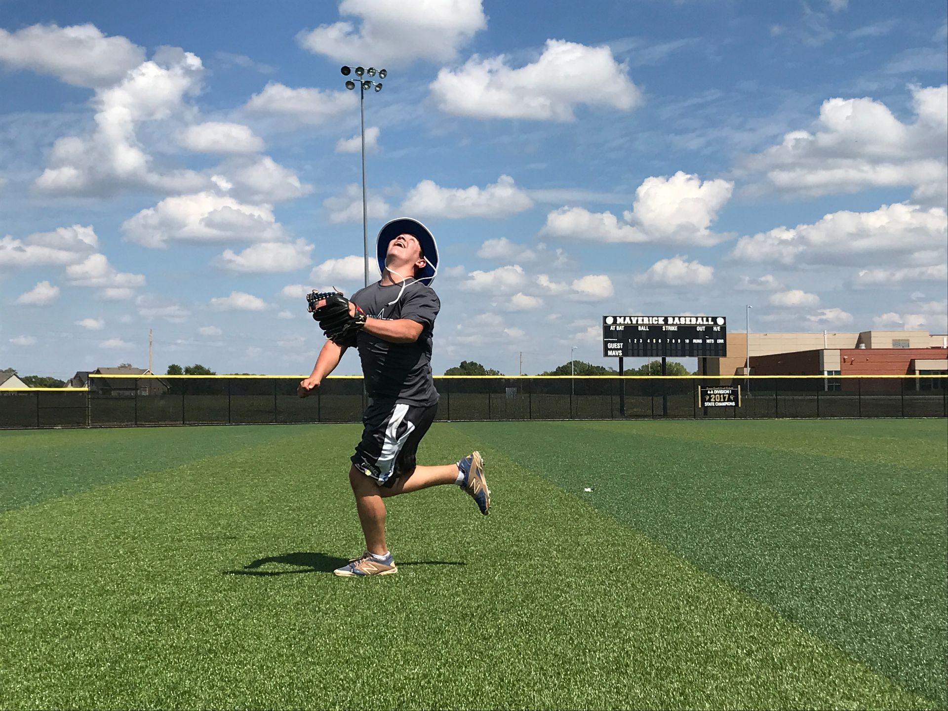 Baseball player in black uniform catching a ball on a sunny field under a blue sky