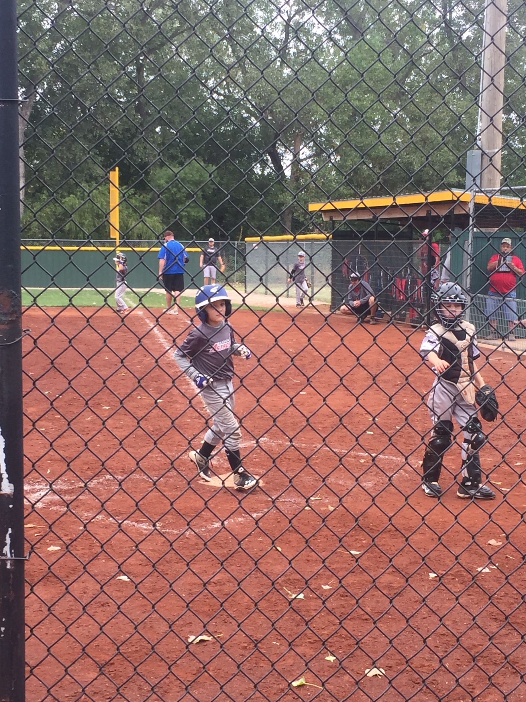 Youth baseball players at bat on a dirt field behind a chain-link fence