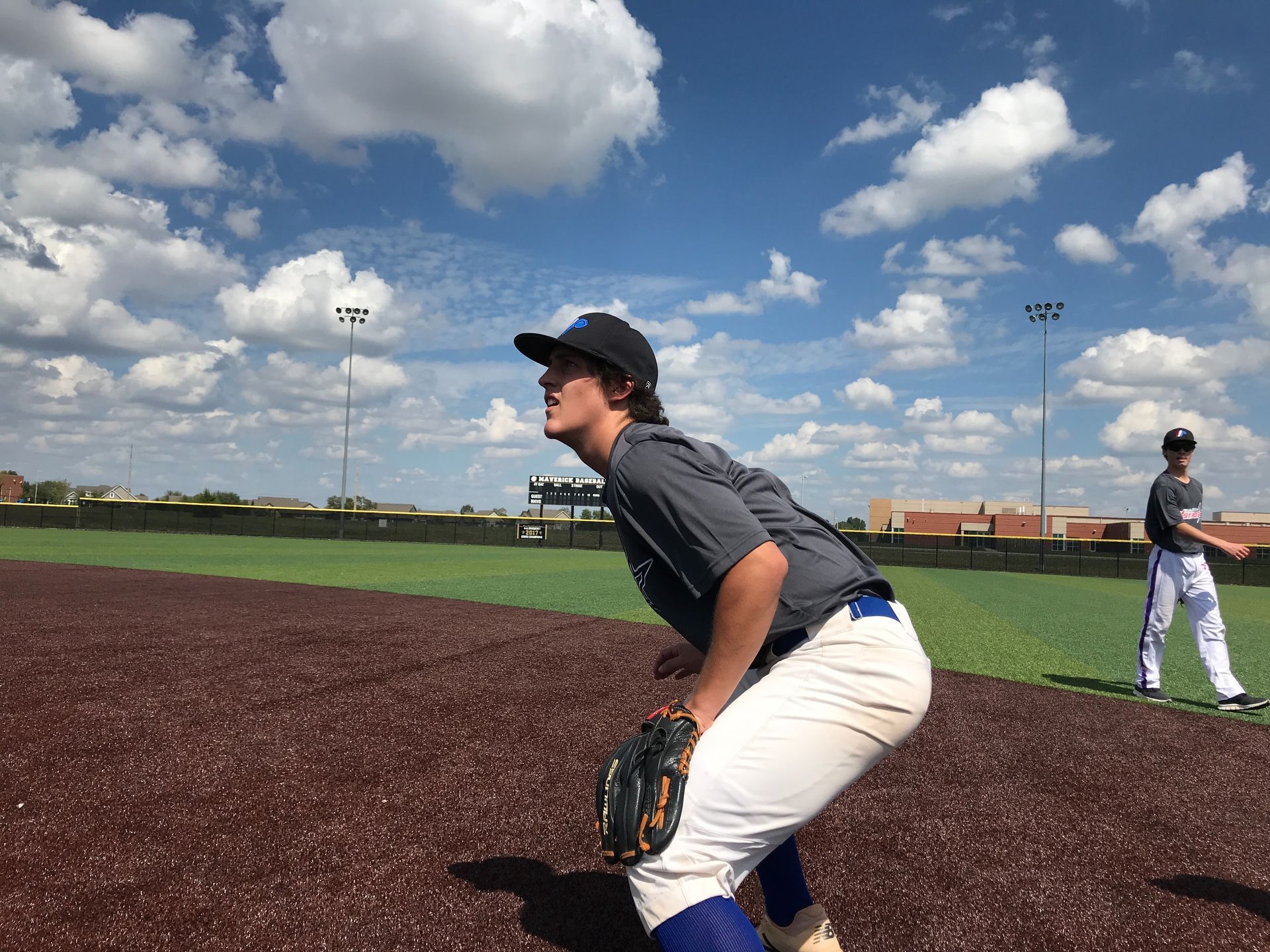 Baseball player in dark jersey and white pants ready in the field under a cloudy sky