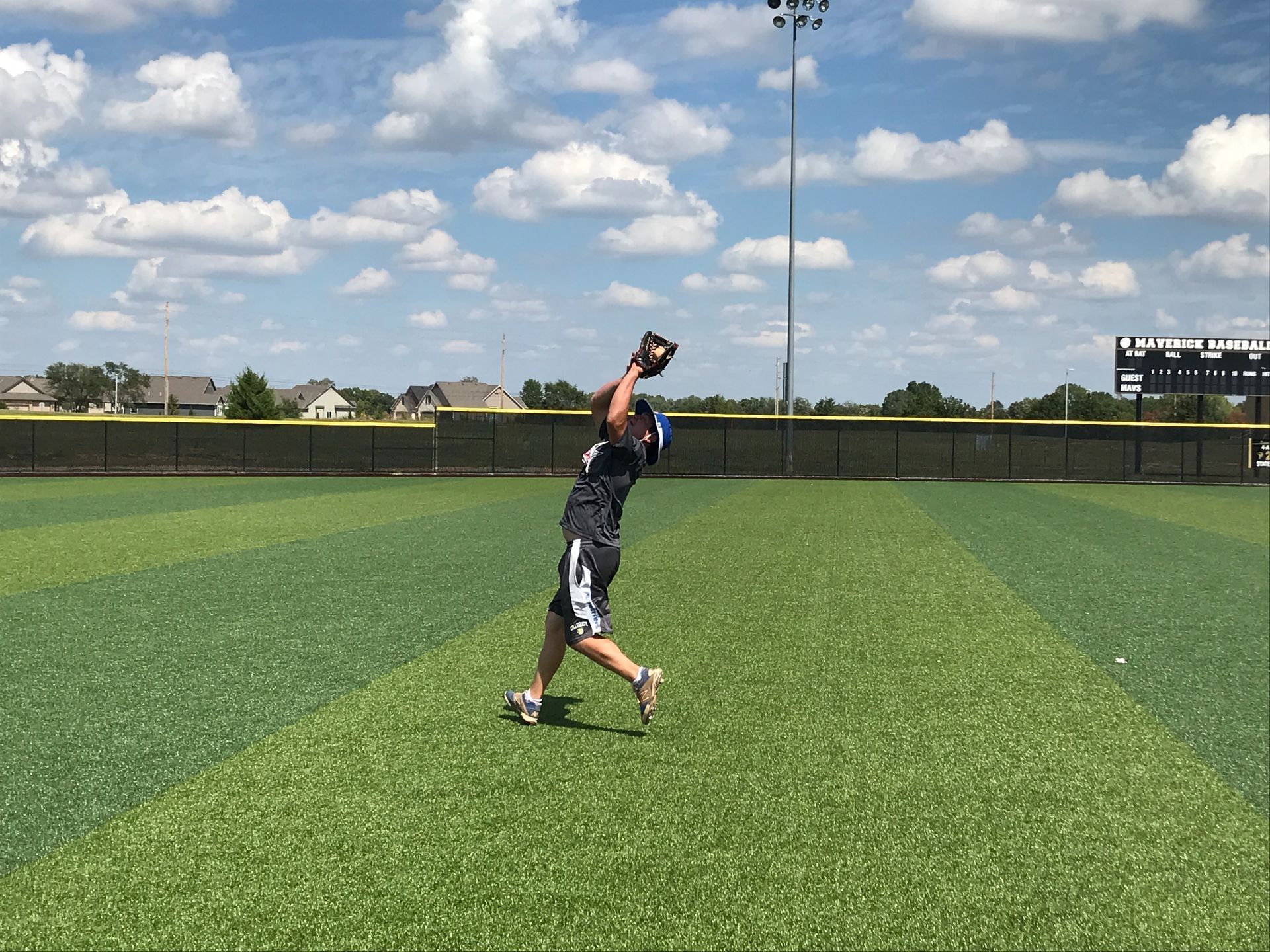 Baseball player catching a fly ball on a green field under a partly cloudy sky