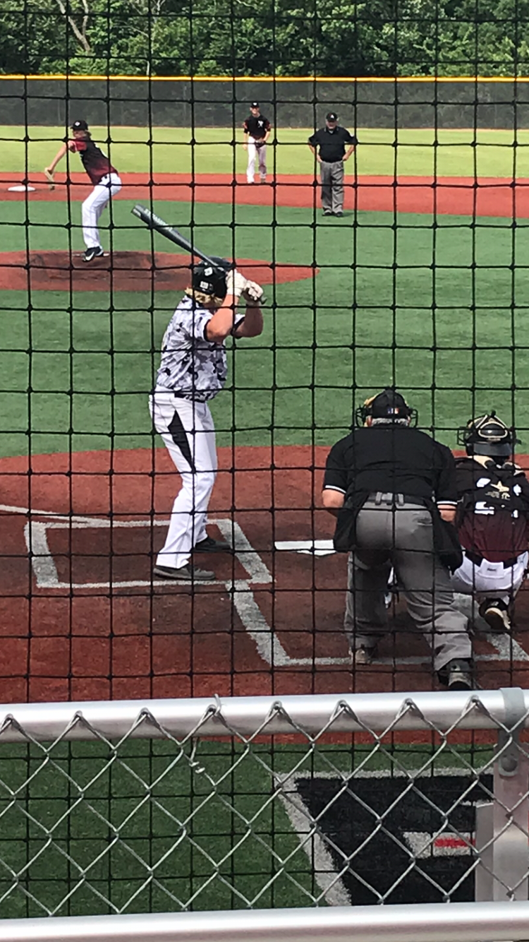 Baseball batter at the plate, pitcher on the mound, with umpire and catcher behind the netting