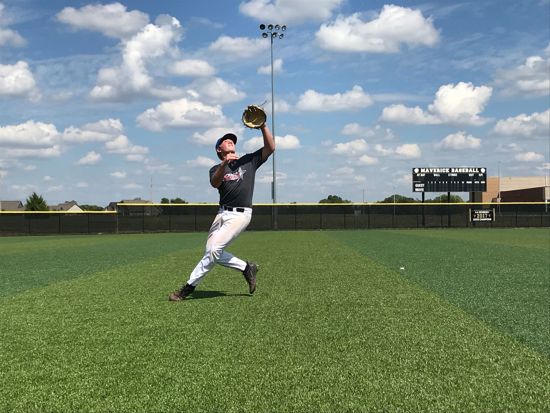 Baseball player leaping to catch a ball on a grassy field under a blue sky