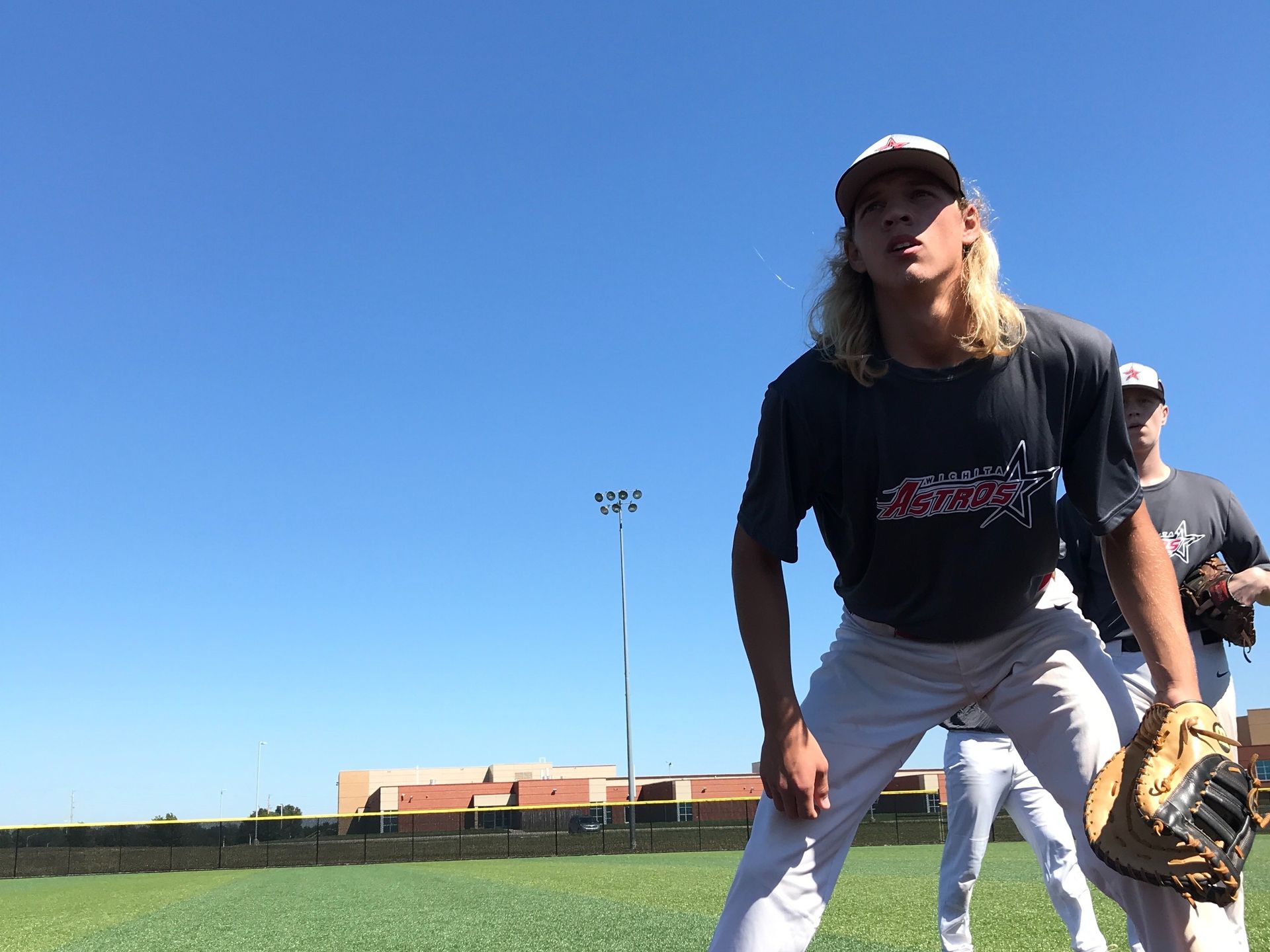 Two baseball players crouch on a field under a clear blue sky.
