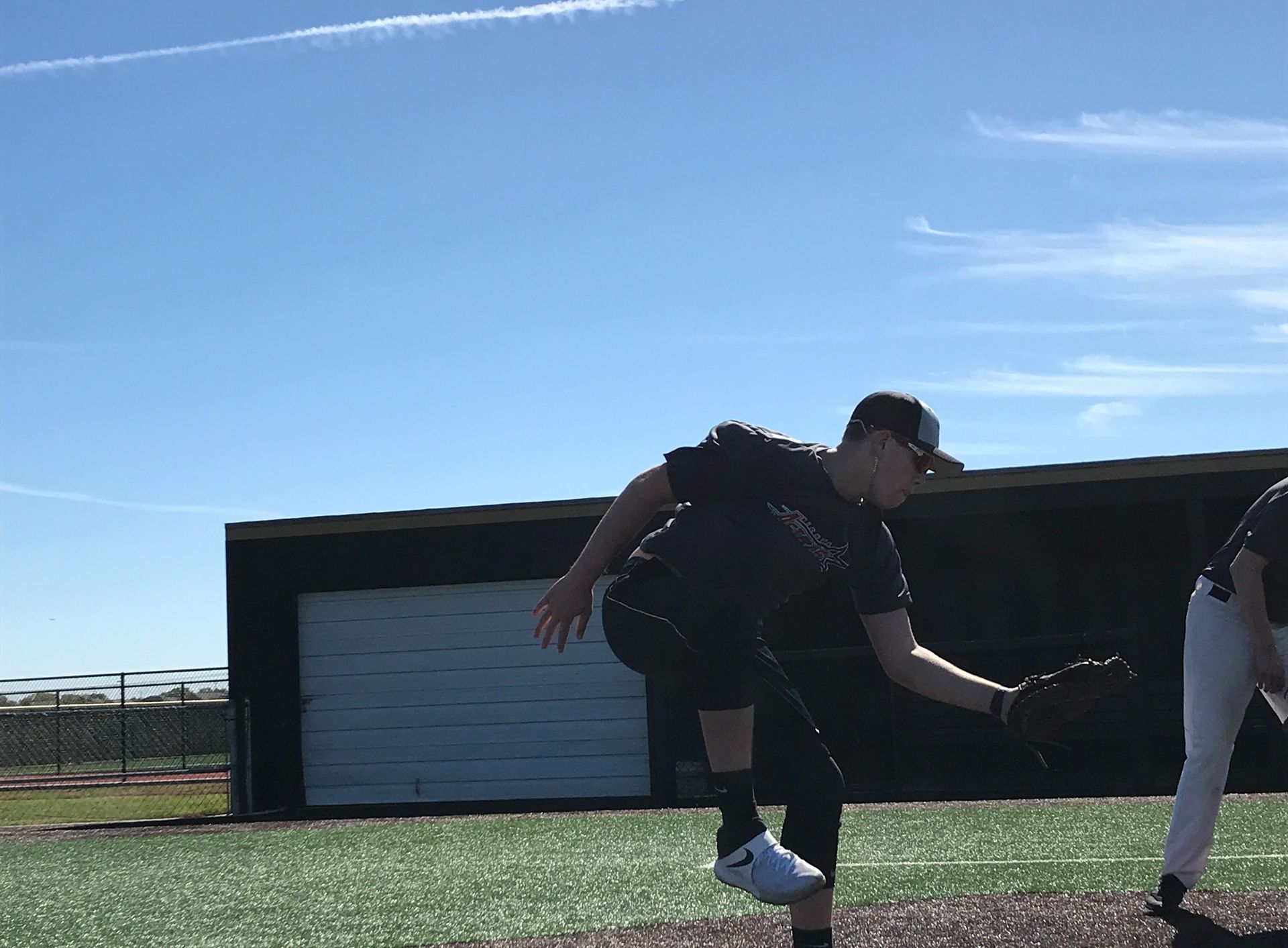 Two people stretching on a field under a clear blue sky, with a building in the background