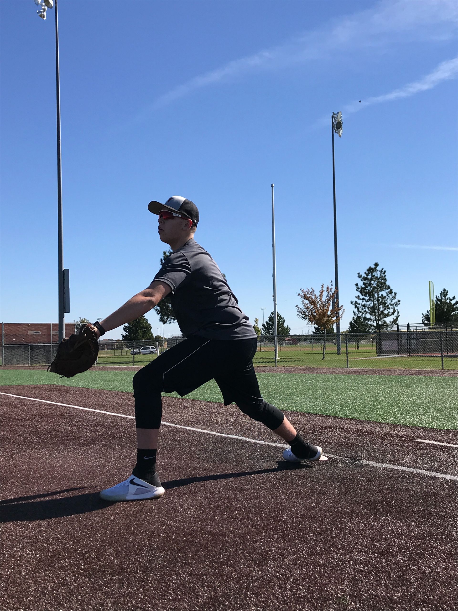 Softball player lunges to catch a ball on a sunny field, wearing a glove and cap.