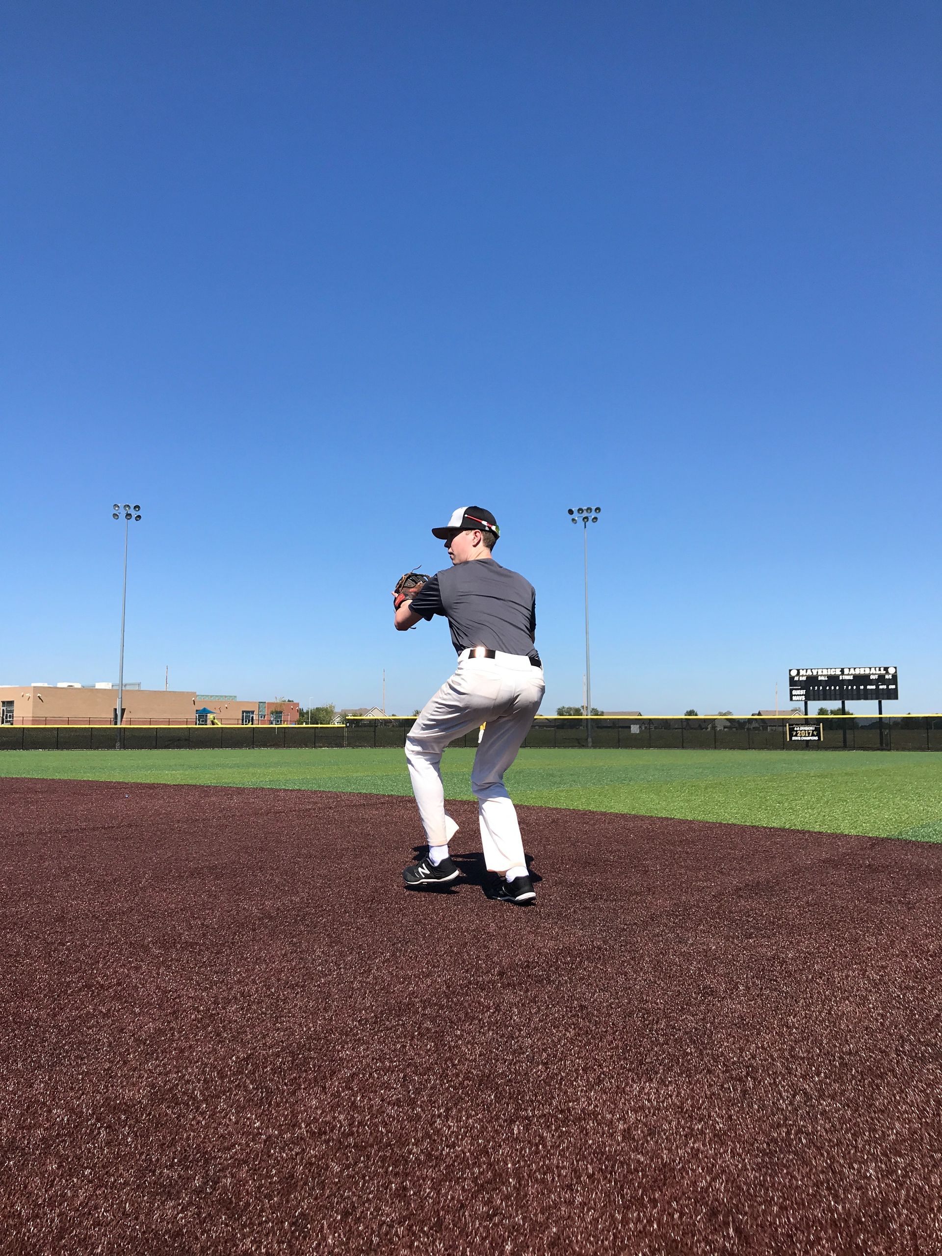 Baseball pitcher mid-throw on a field under a clear blue sky