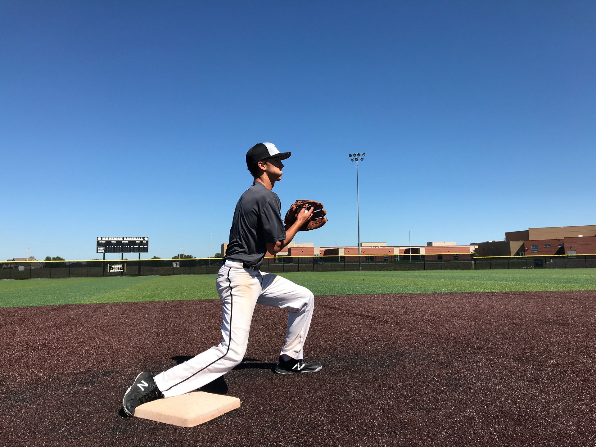 Baseball player in dark uniform stretching on the field near a base under a clear blue sky