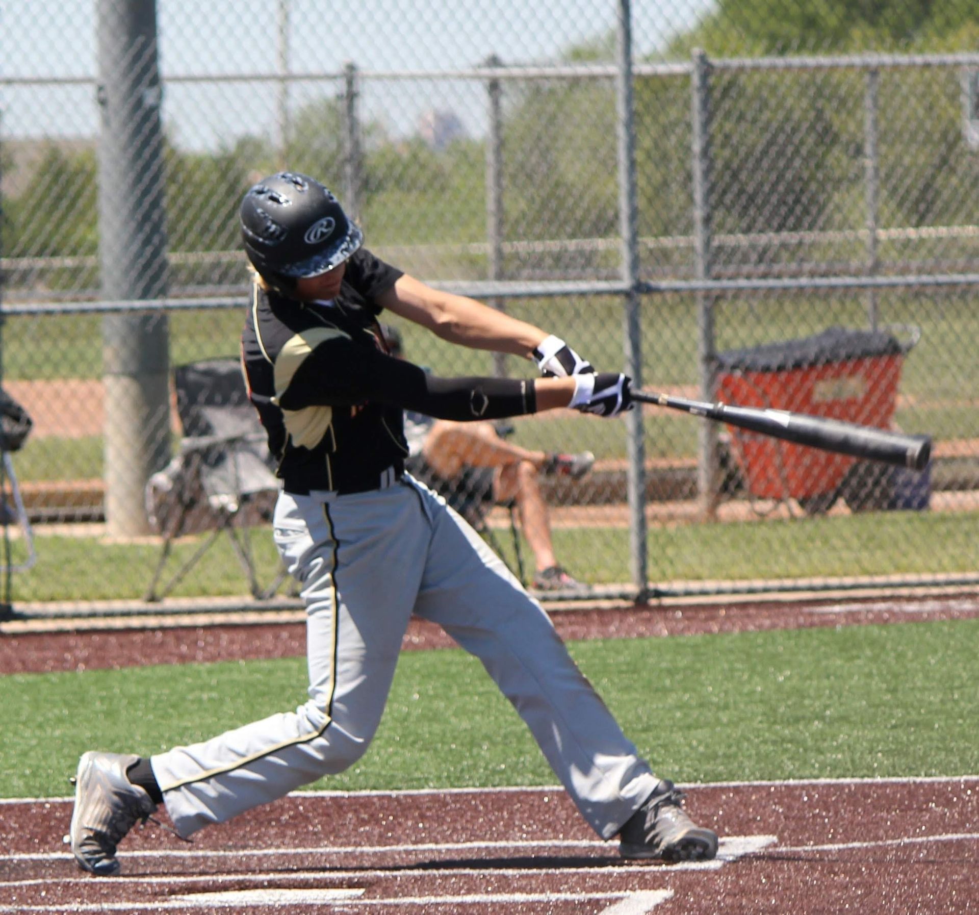 Baseball player in black and gray swings a bat at a ball on a sunny field