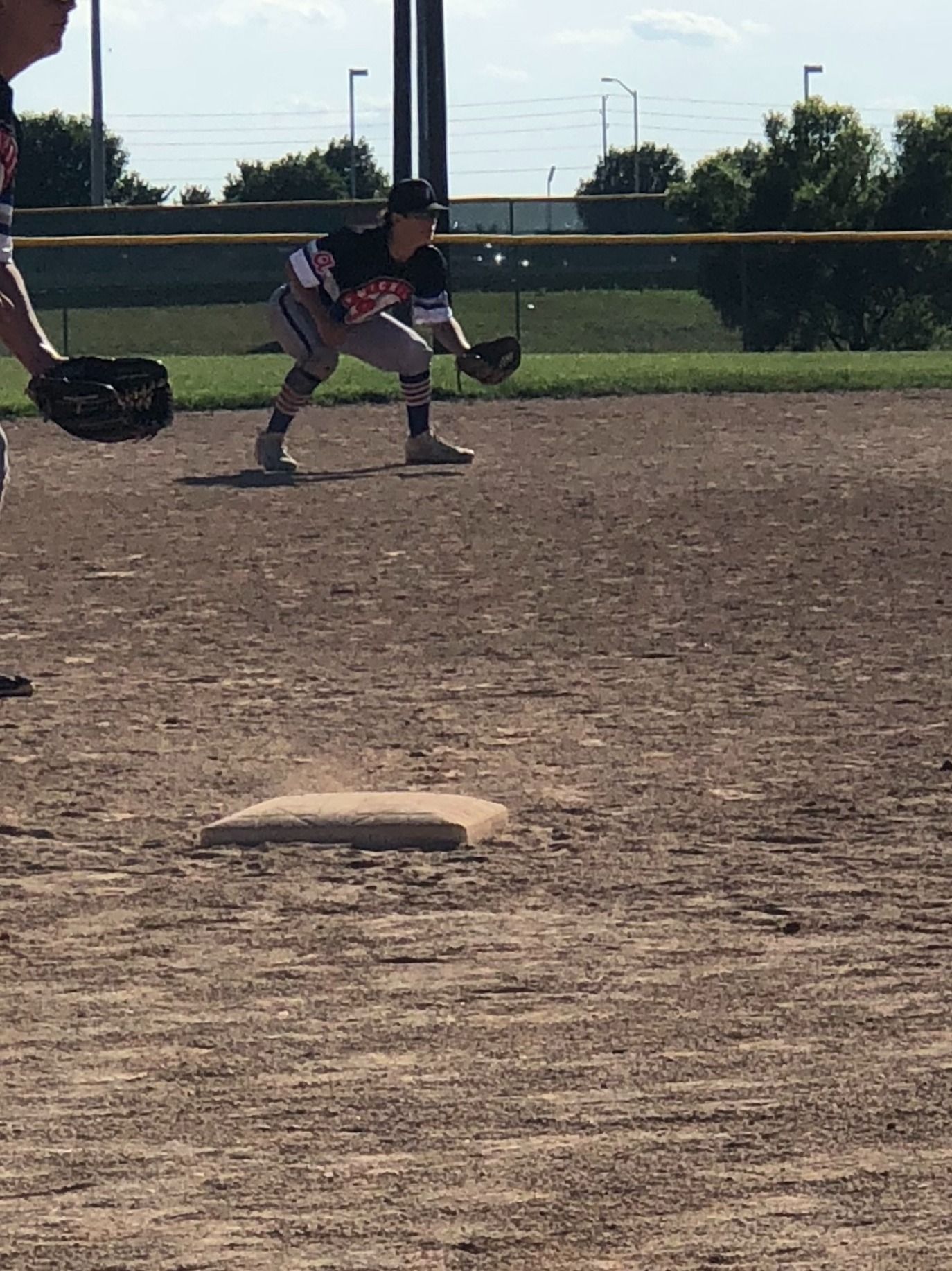 Youth baseball player crouches in the infield, glove ready near a base on a sunny field.