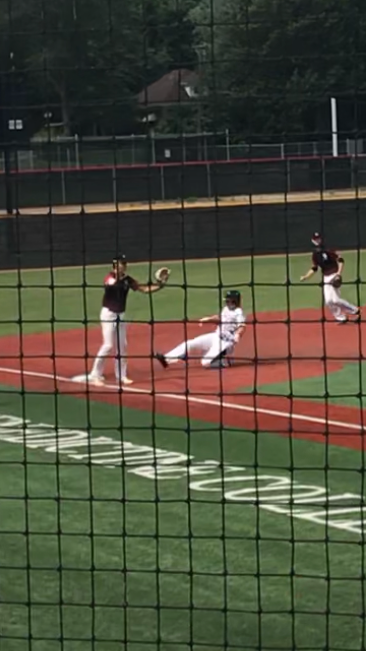 Baseball players at a base, with one sliding and another reaching with a glove on the infield.