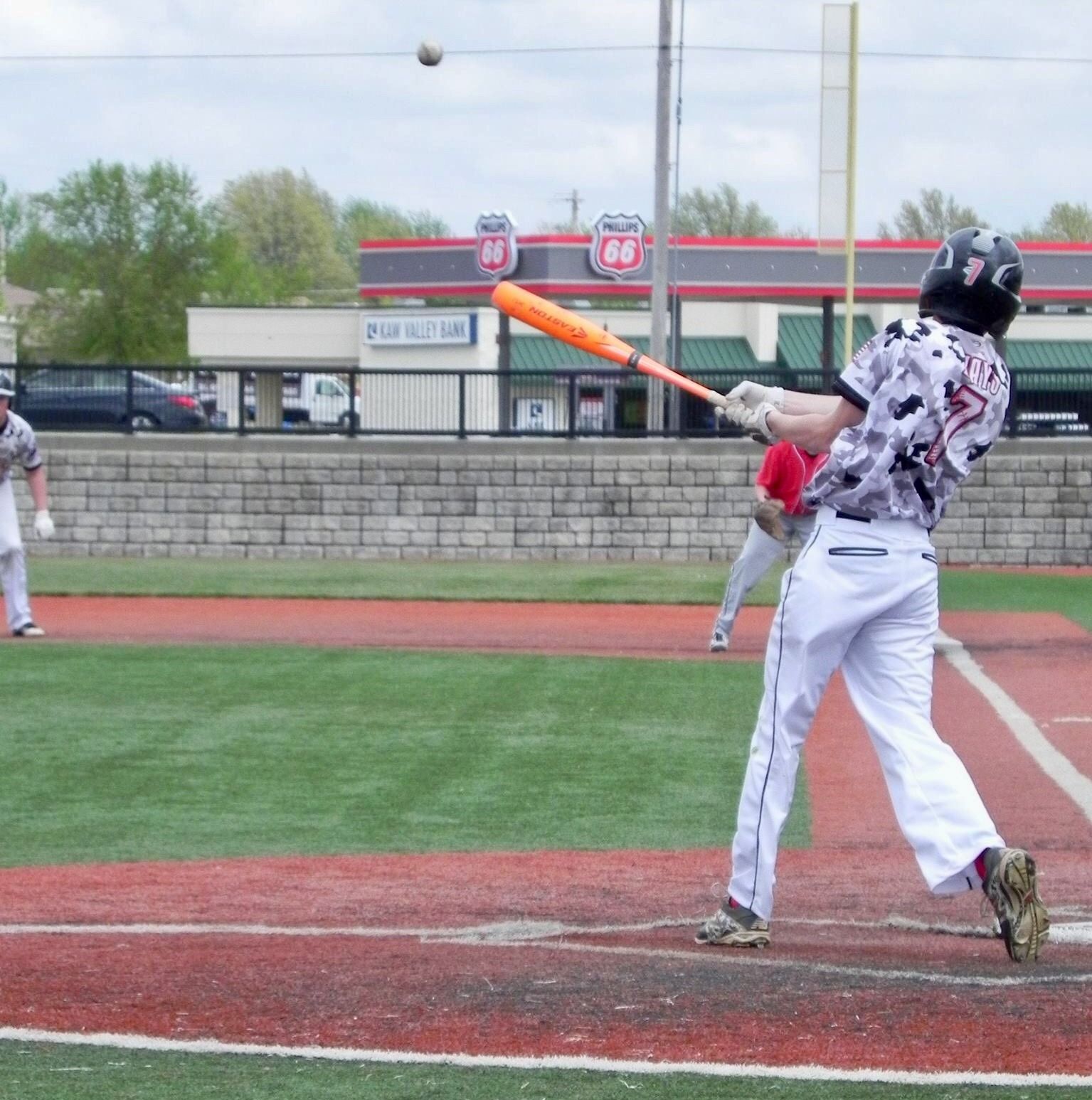 Baseball batter in white uniform swings at a pitch on a field, with ball in midair.
