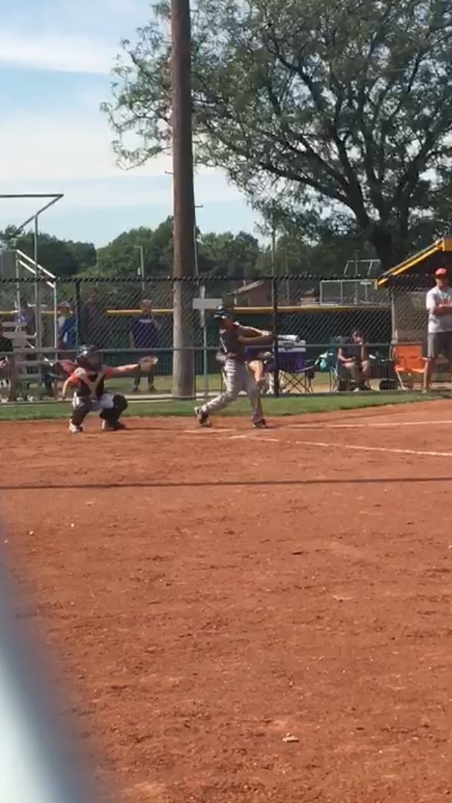 Baseball field with a catcher crouched by home plate and players on the bench behind a fence