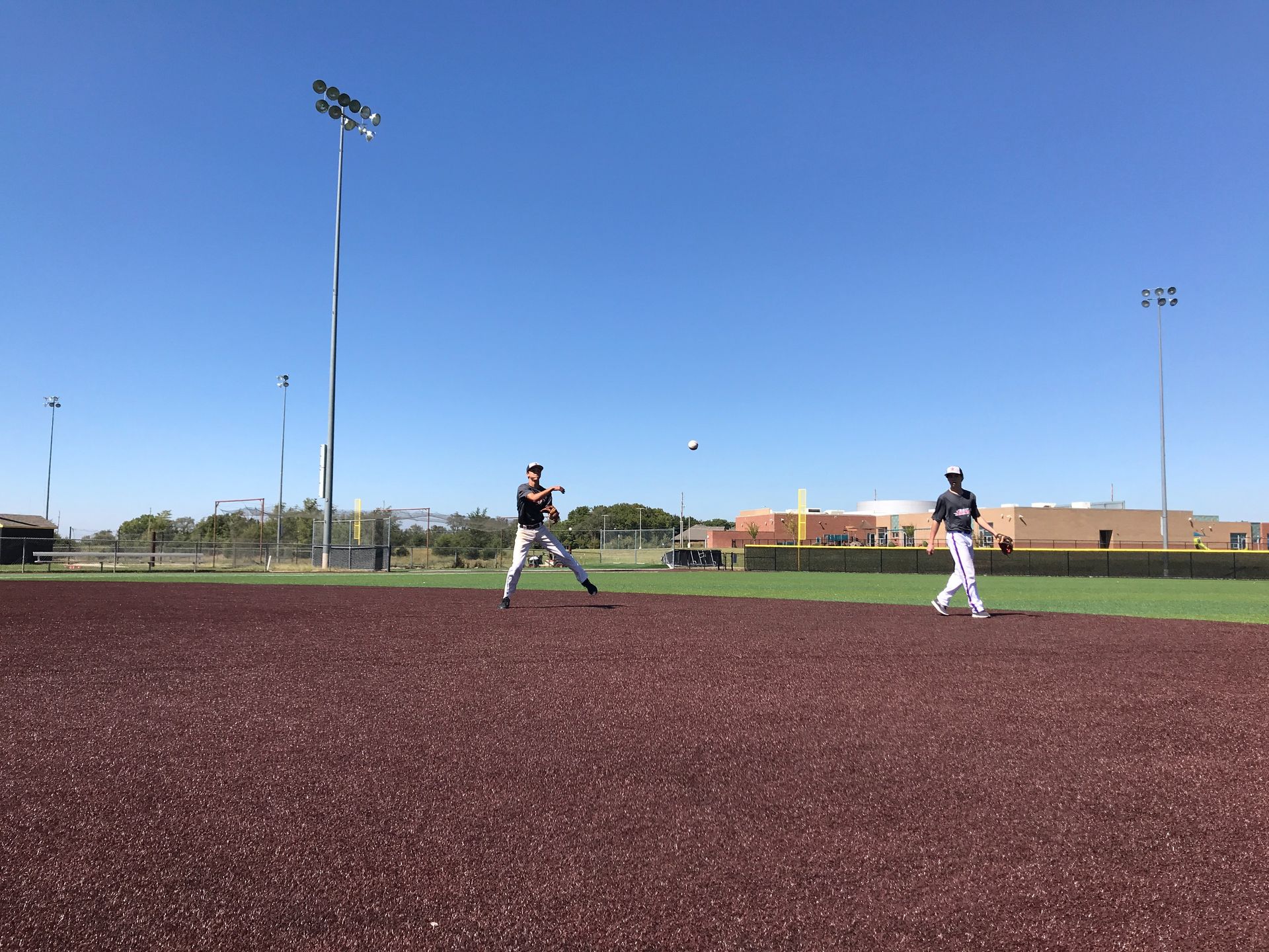 Two baseball players on a maroon field under a clear blue sky with stadium lights.