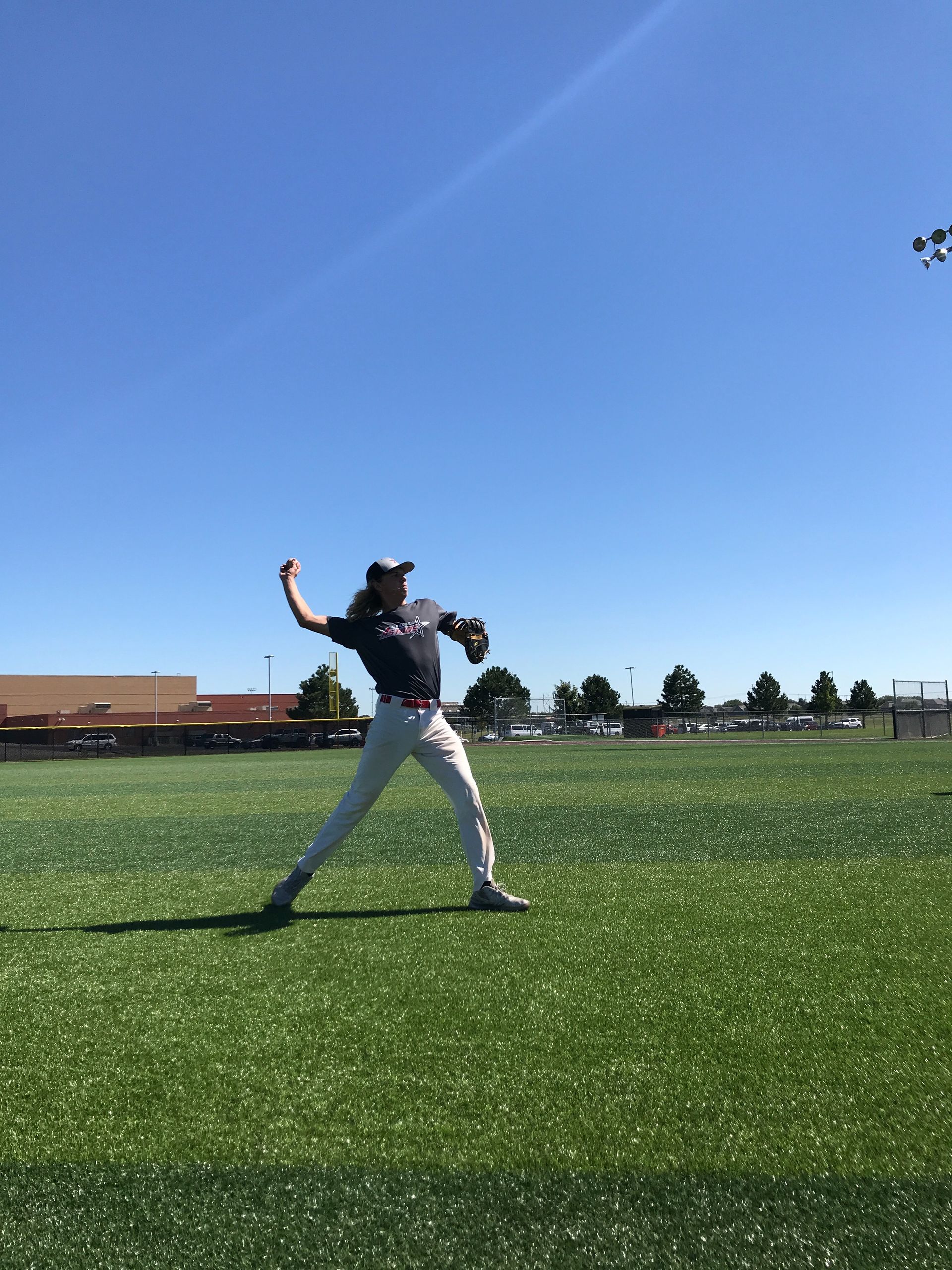 Person pitching a baseball on a sunny field under a clear blue sky
