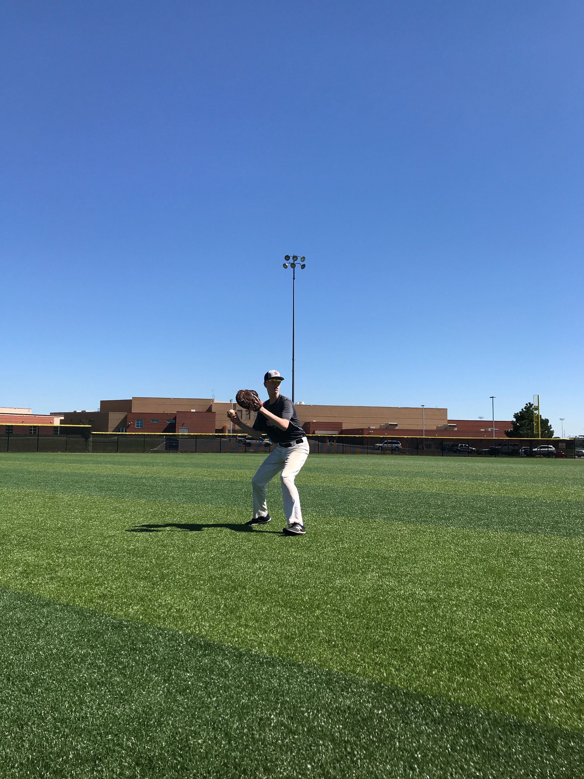 Baseball player in white uniform ready to catch on a green field under a clear blue sky.