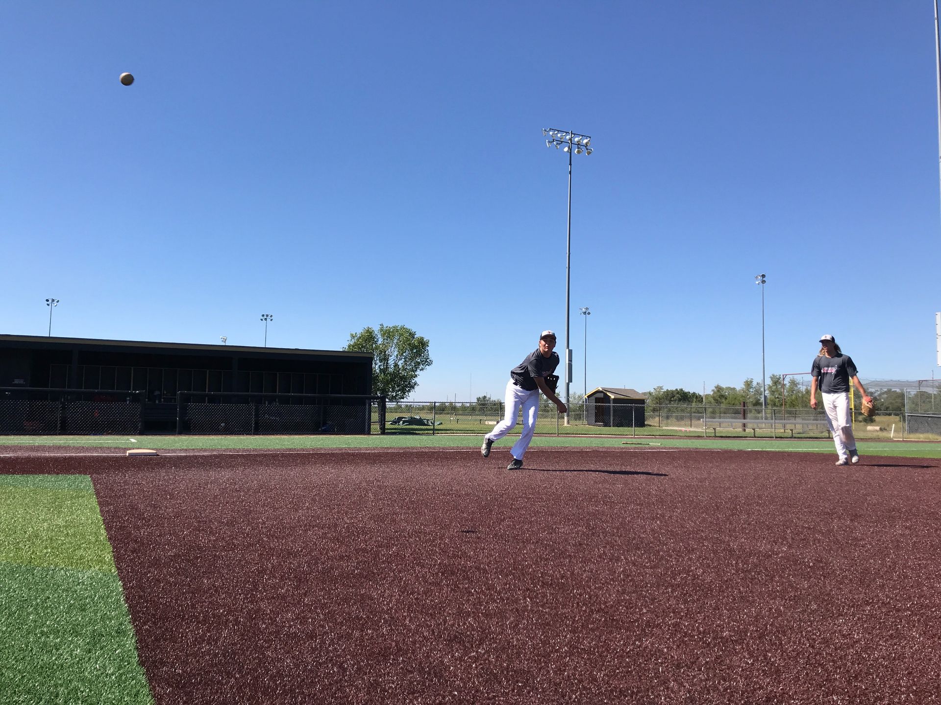Two people play on a baseball field under a clear blue sky, one running on the infield.