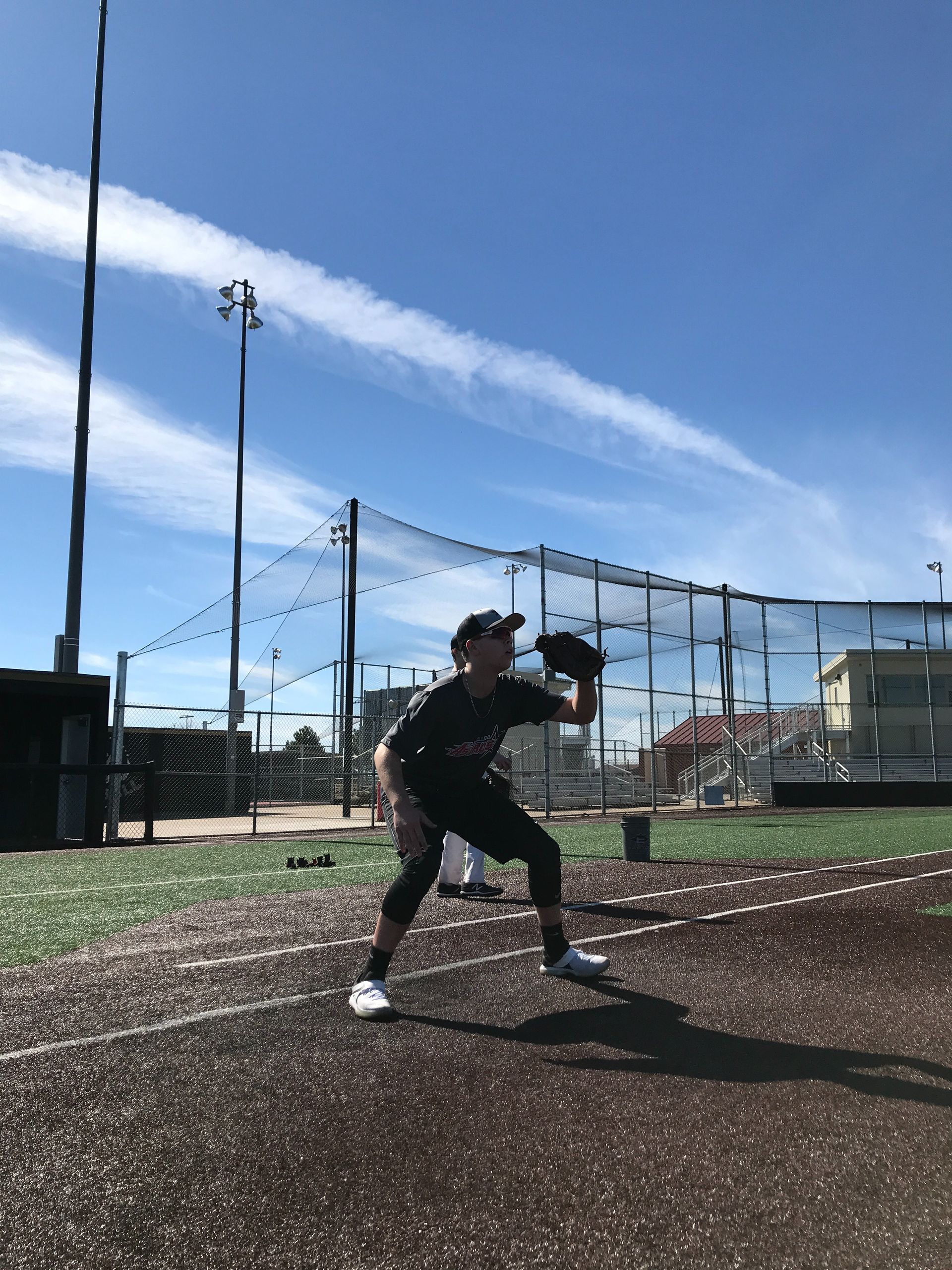 Baseball player in black uniform warming up on a field under a blue sky