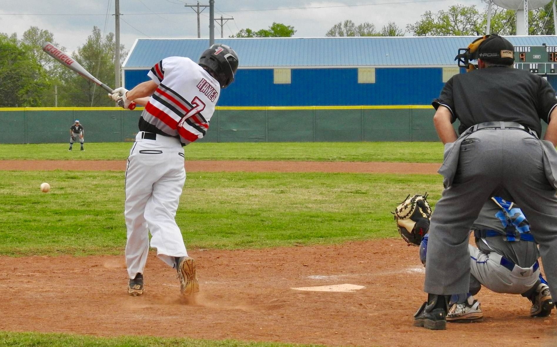 Baseball batter swings at home plate as catcher and umpire watch on a rainy field