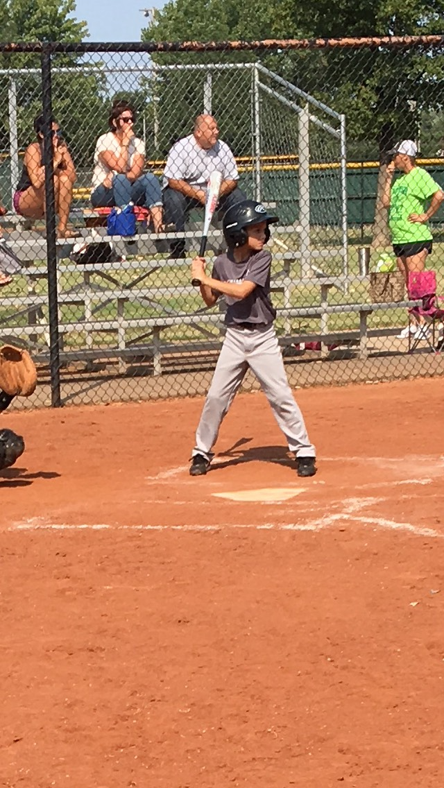 Young baseball player at bat on a clay field, with spectators behind the fence.