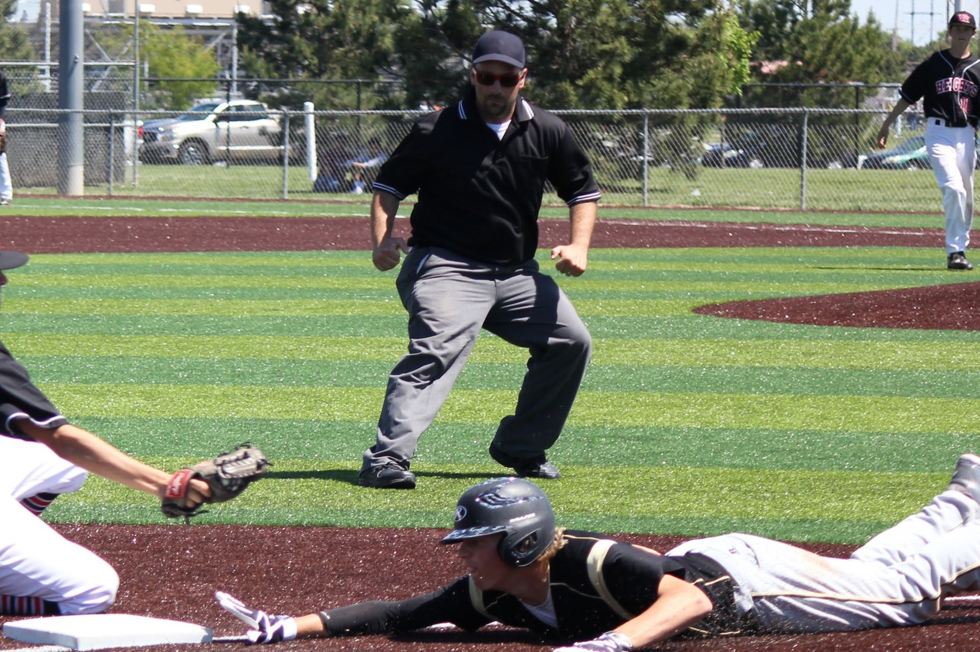 Baseball player slides into home plate as catcher and umpire watch on the field.