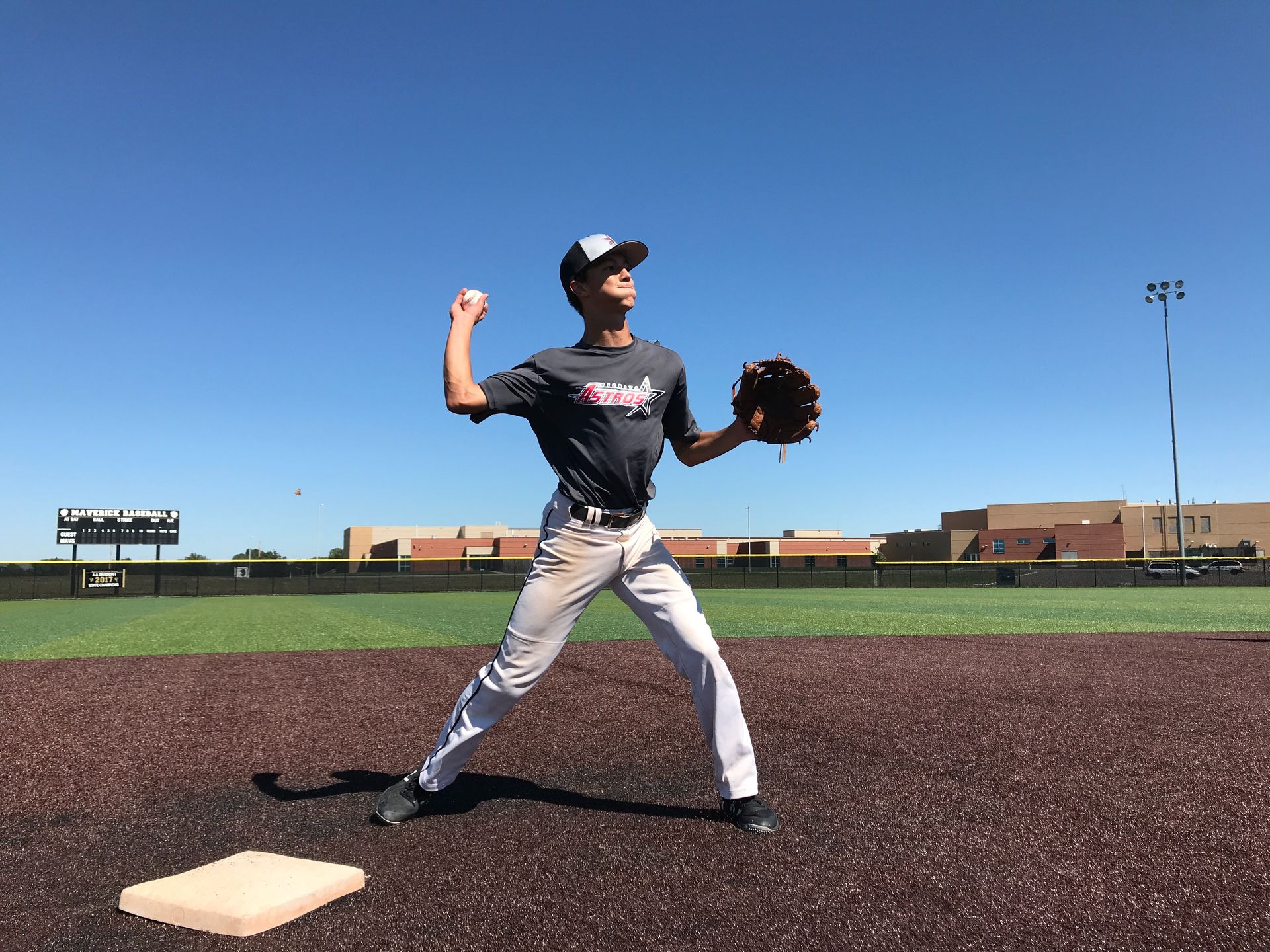 Baseball pitcher in gray uniform mid-throw on a field under a clear blue sky