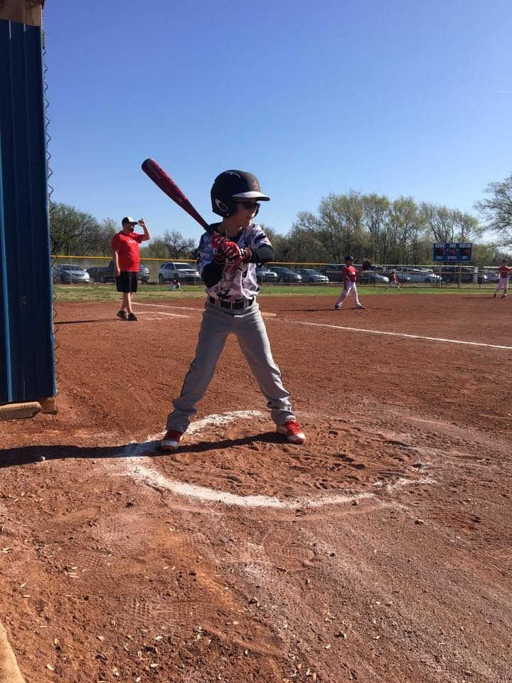 Young baseball player at home plate holding a bat, ready to swing on a sunny field.