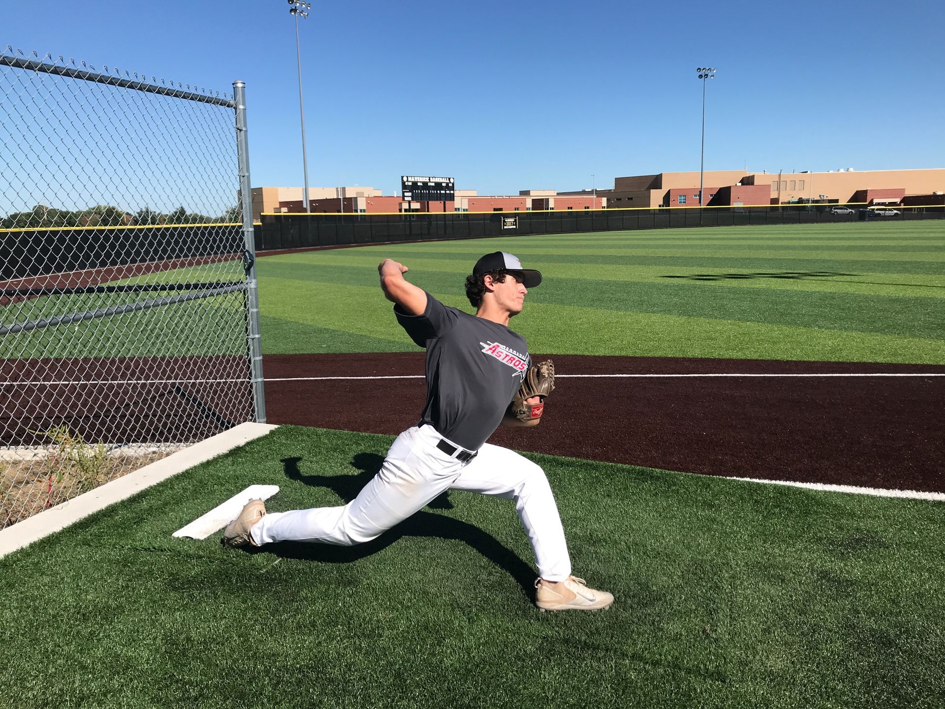Baseball player in gray uniform mid-pitch on a field under bright daylight