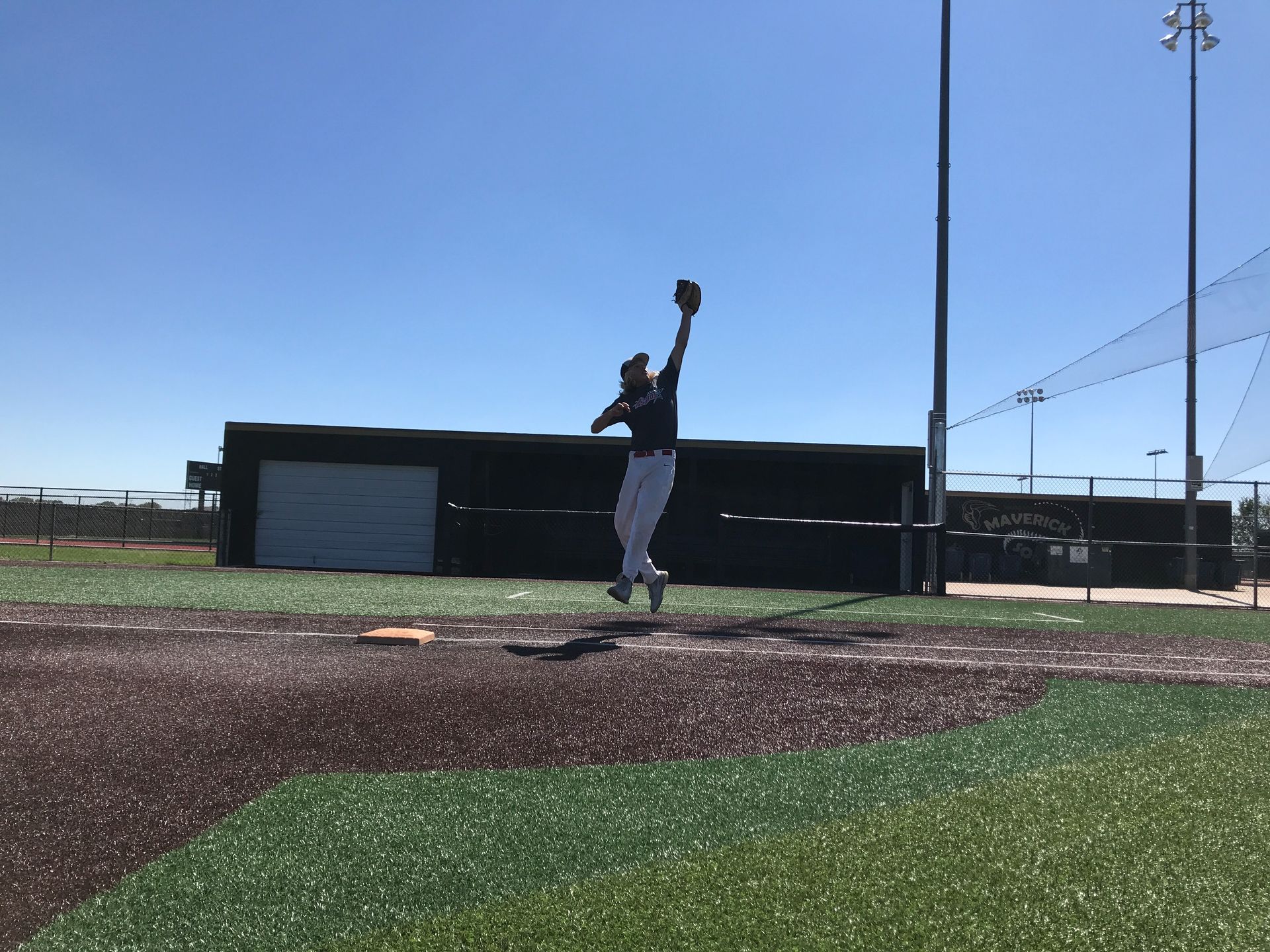 Baseball pitcher mid-throw on a field under a clear blue sky