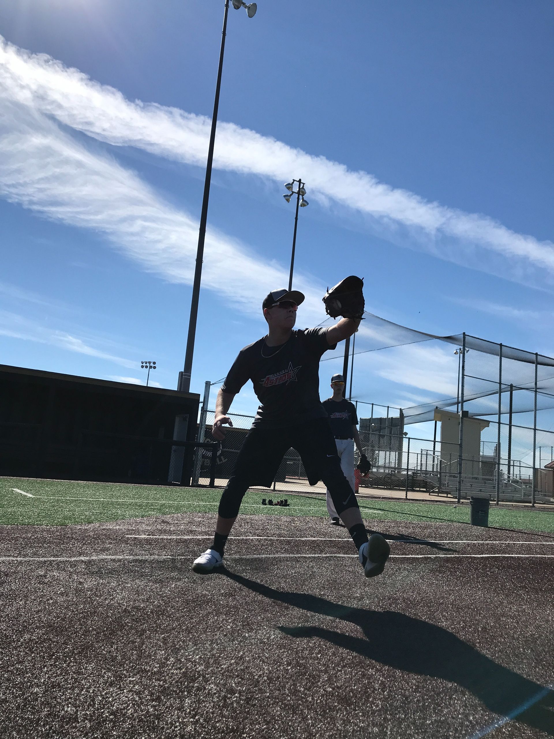 Baseball player in dark uniform holding a glove on a sunny field under a blue sky