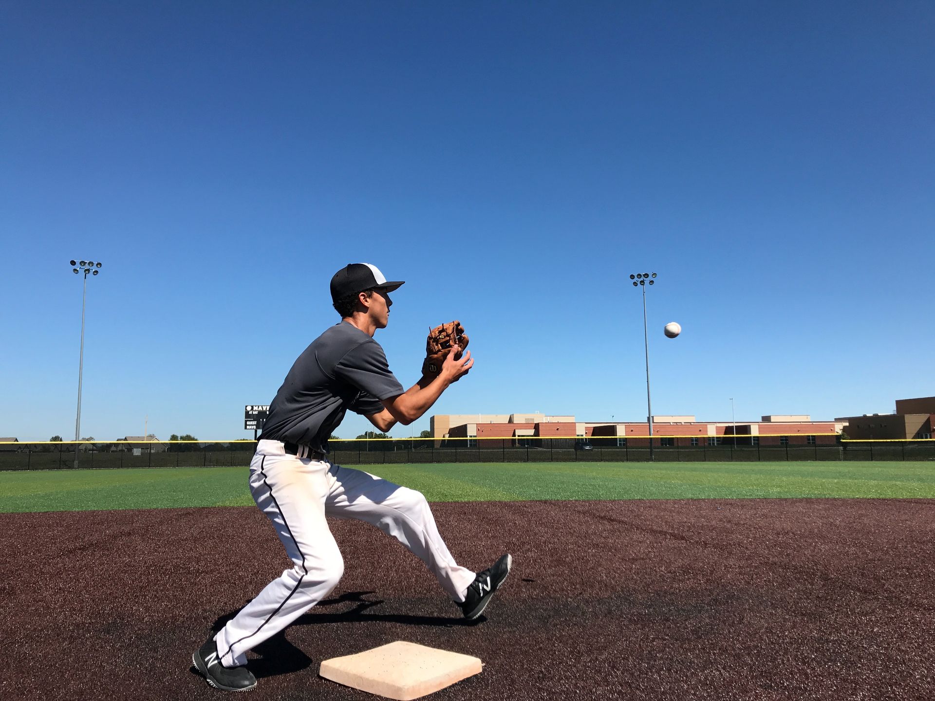 Baseball player in dark uniform catching a ball on a sunny field under a clear blue sky