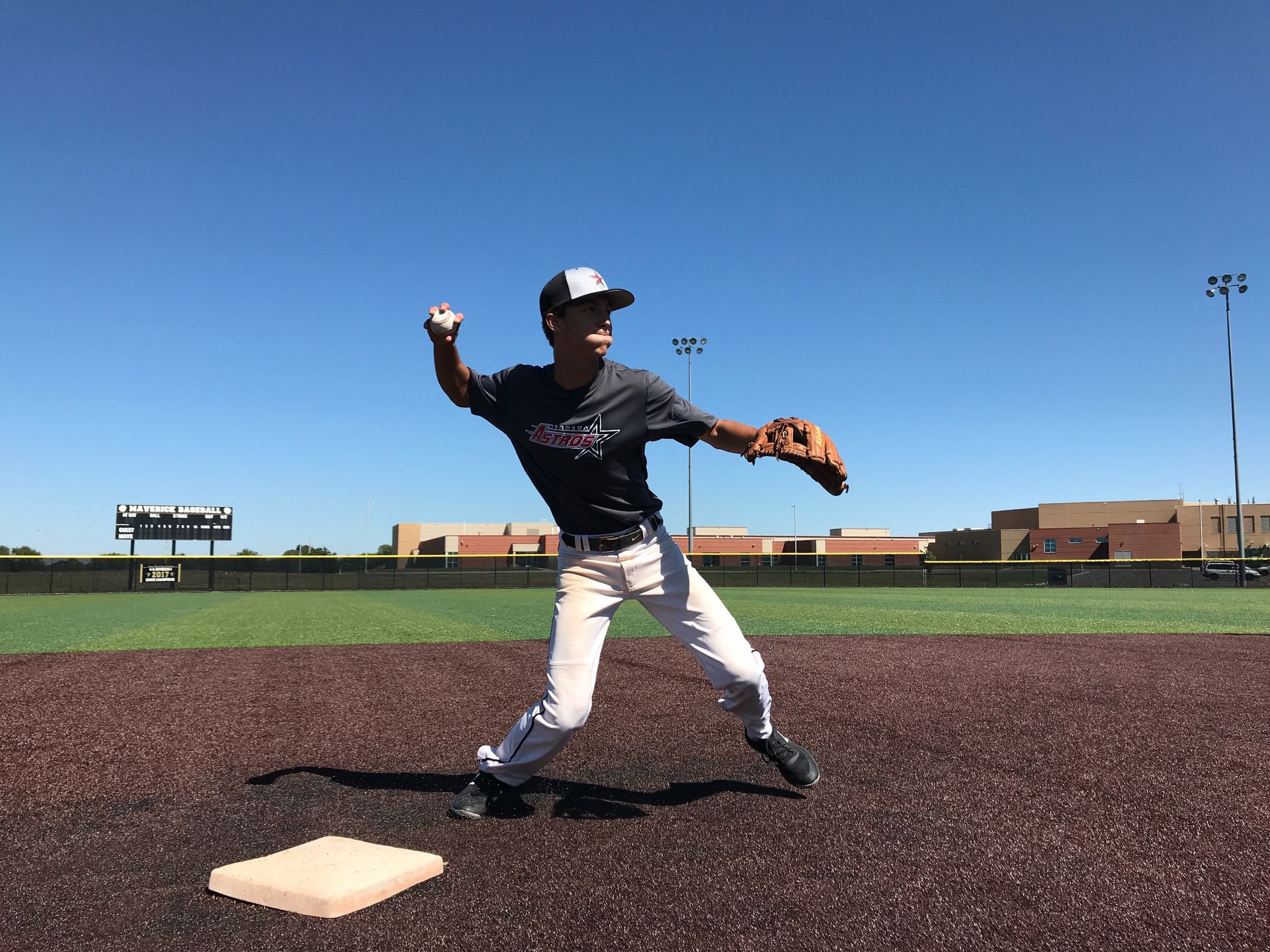Baseball player in white pants and dark jersey fields a ball on a sunny field near first base.