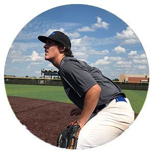 Baseball player in gray uniform crouches on field under a blue sky with clouds