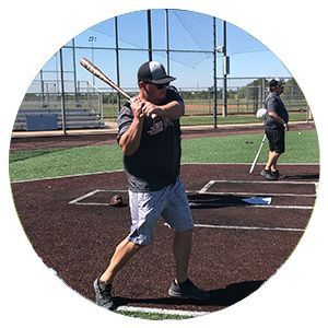 Baseball player holding a bat in a batting cage on a sunny field
