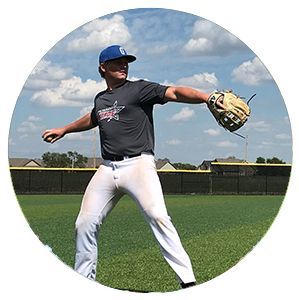 Baseball player in a gray shirt and white pants, mid-throw on a grassy field under a cloudy sky