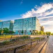 A large building with a lot of windows is surrounded by trees and a fence.