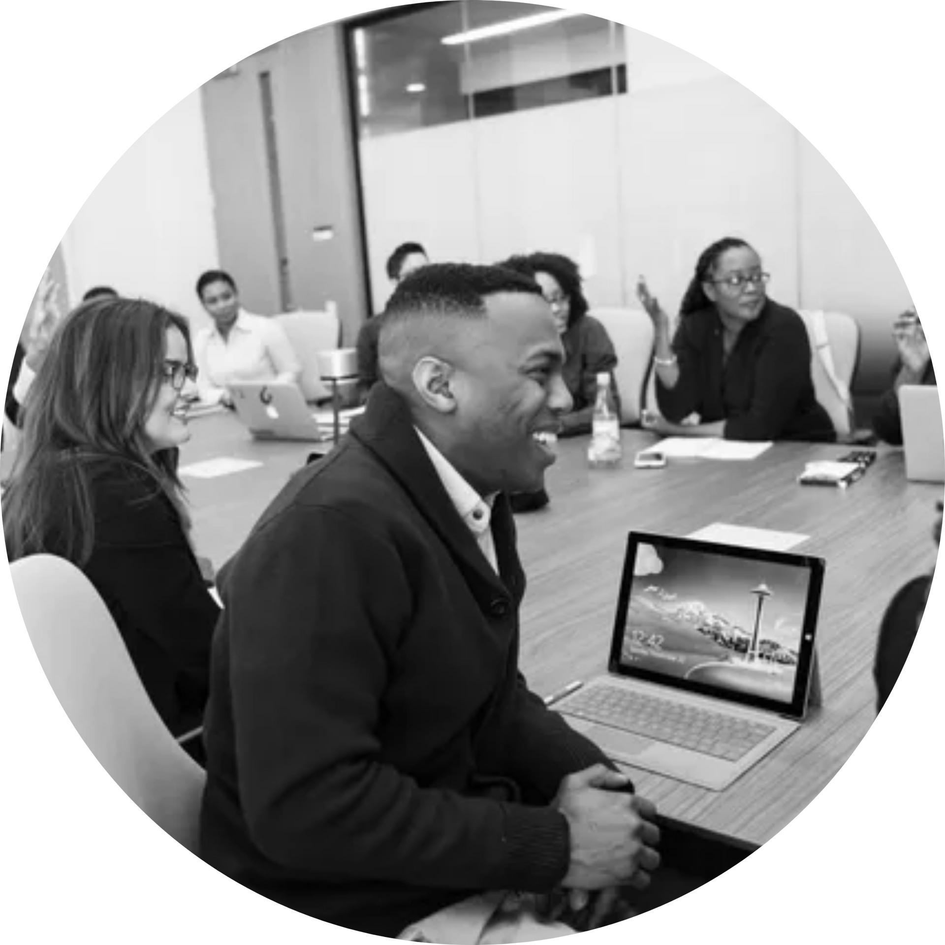 A group of people are sitting around a conference table with laptops.