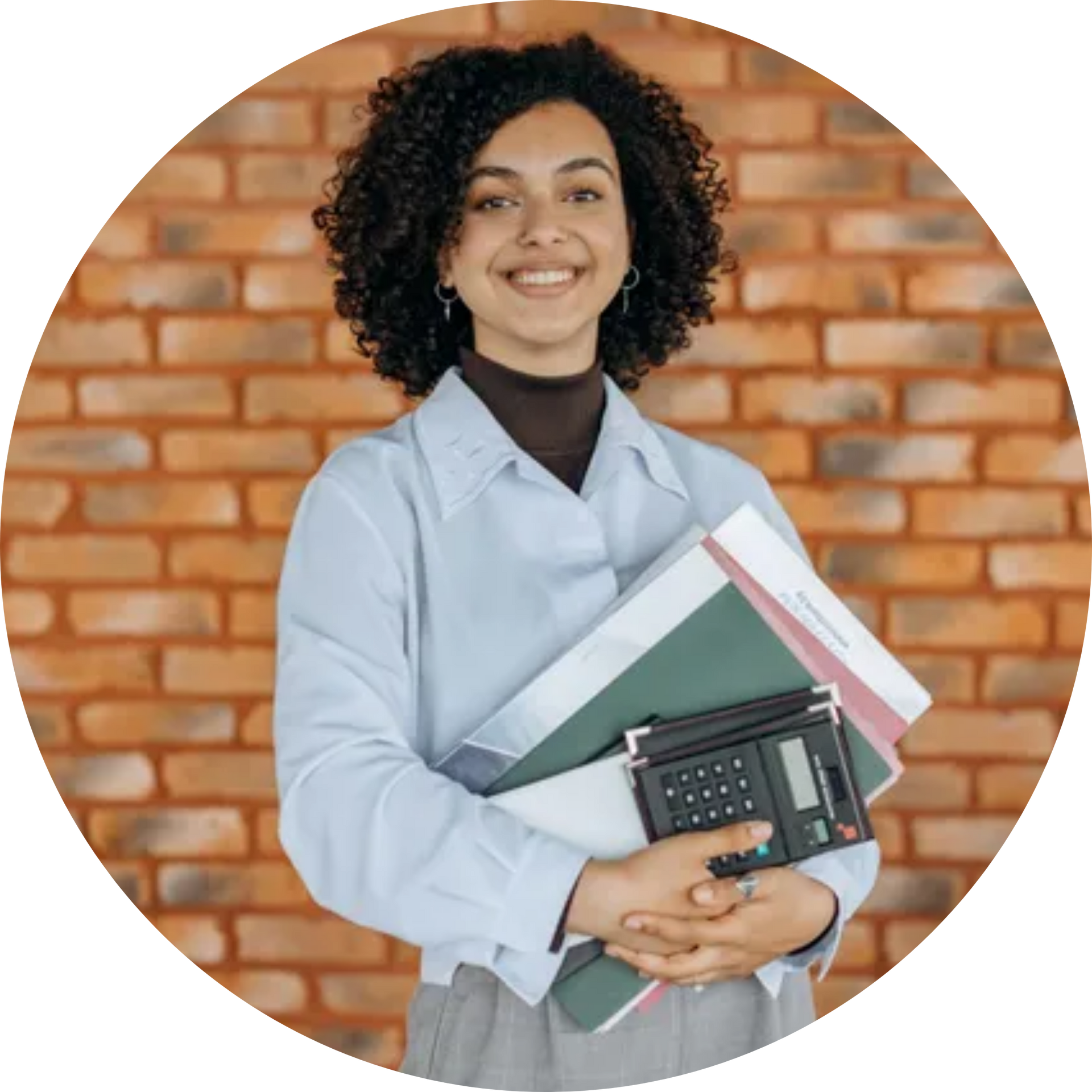 A woman is holding a stack of books and a calculator in front of a brick wall.