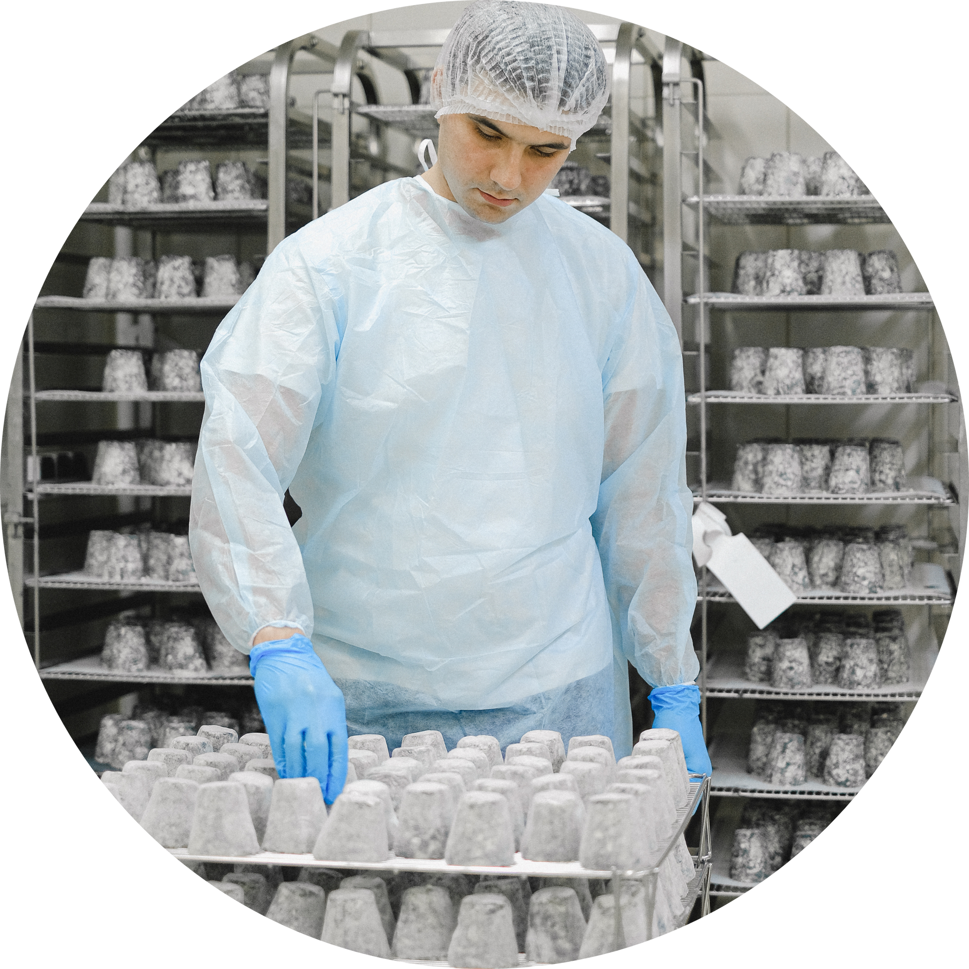 A man wearing a surgical gown and blue gloves is working in a factory with food