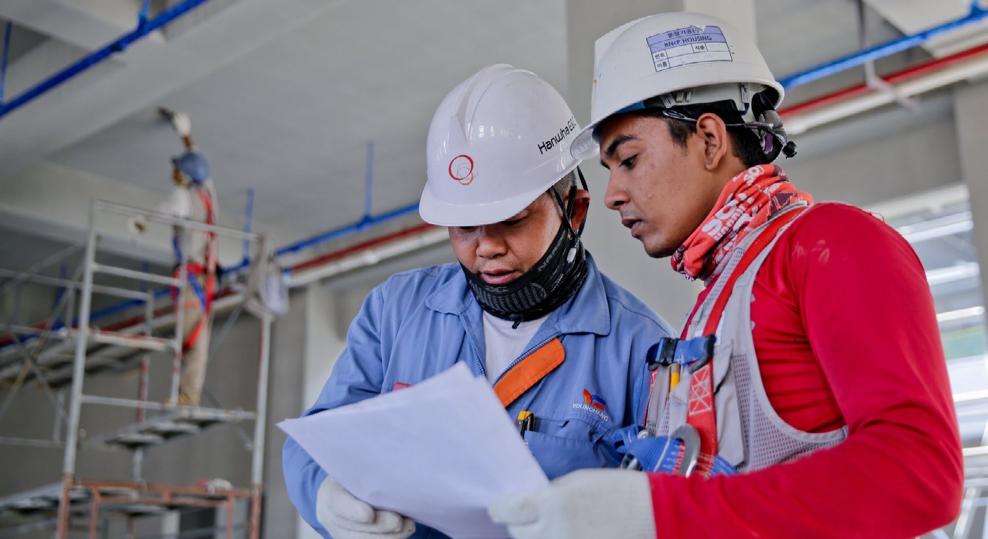 Two construction workers are looking at a piece of paper on a construction site.