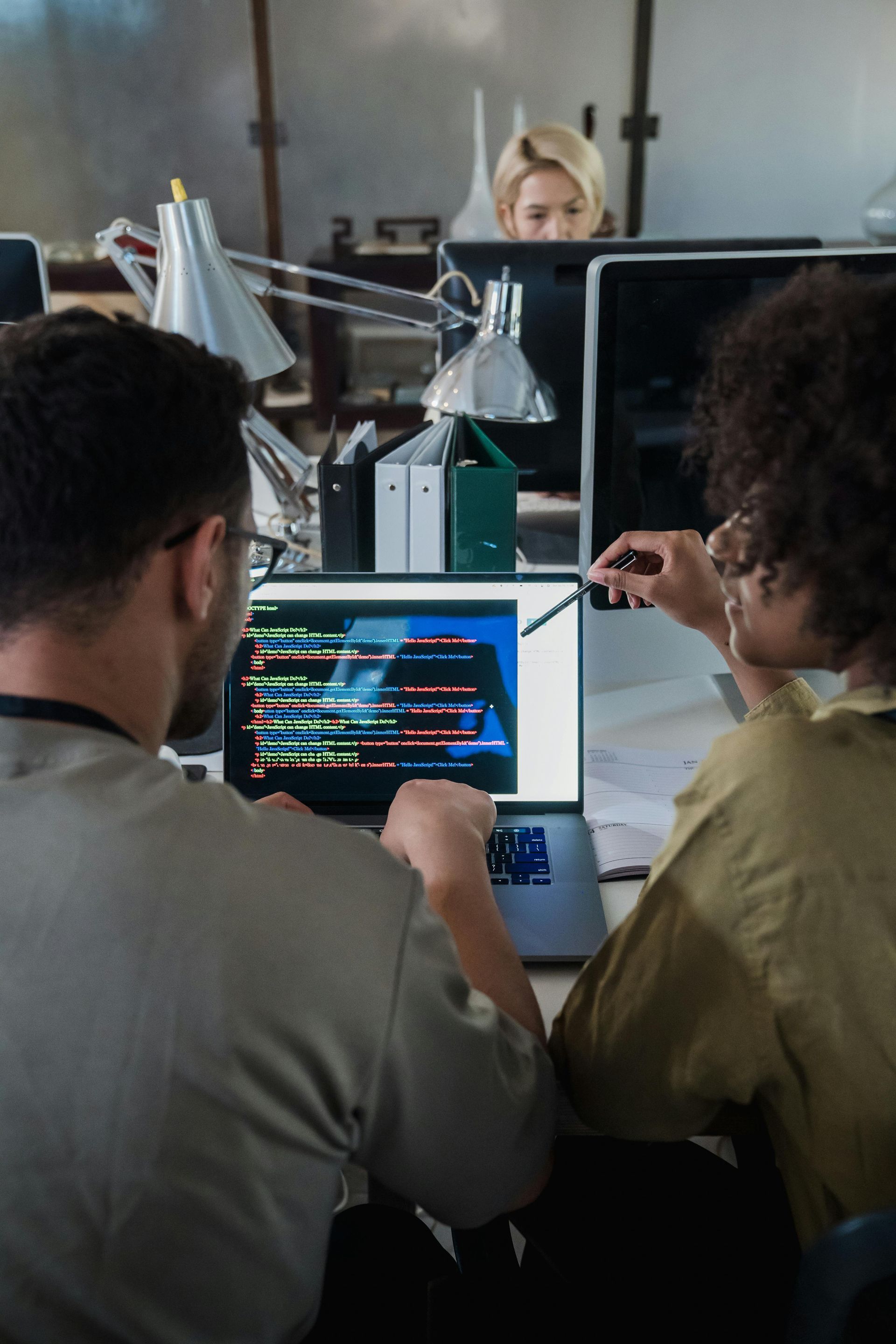 A man and a woman are sitting at a desk looking at a laptop screen.