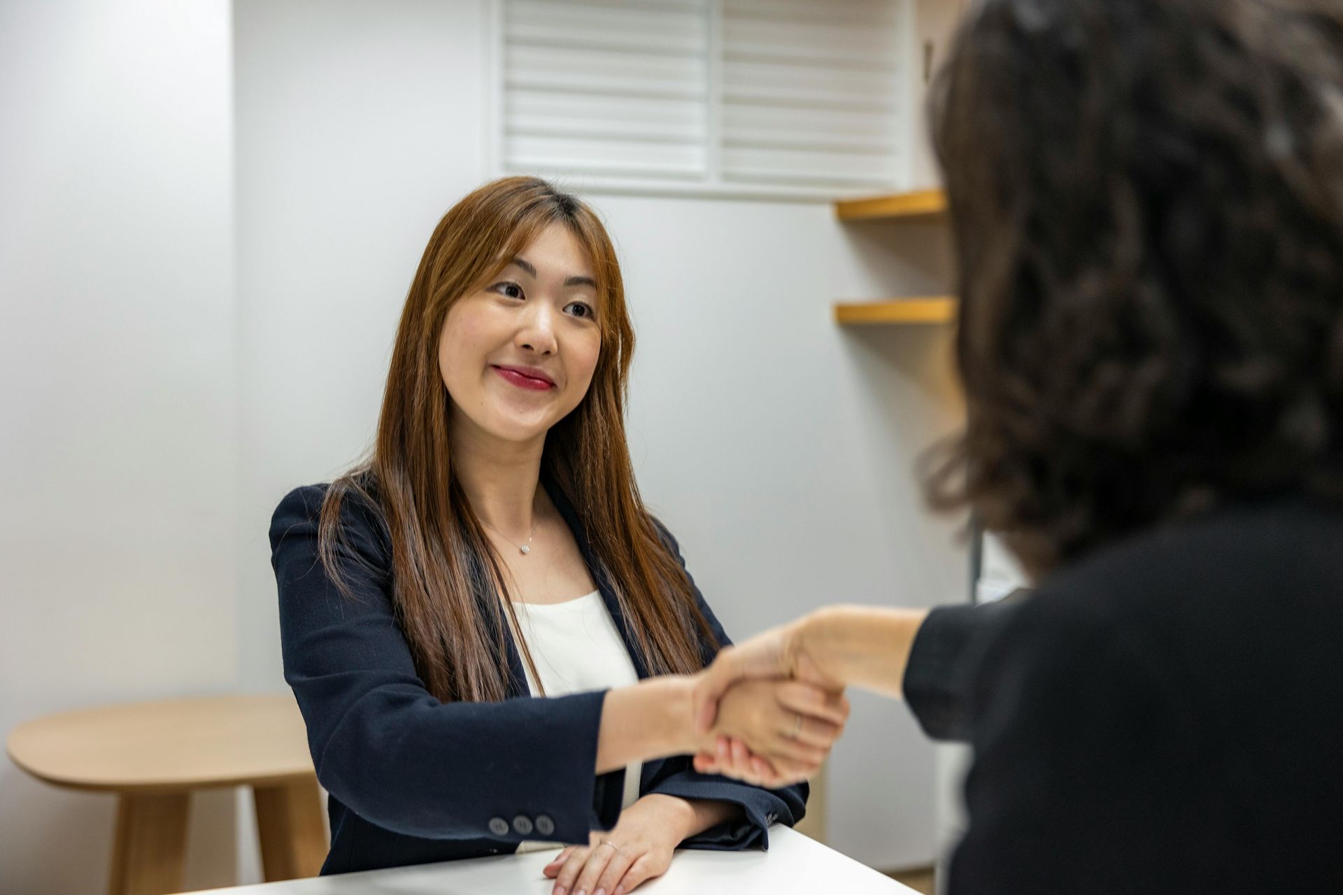 A woman is shaking hands with another woman while sitting at a table.