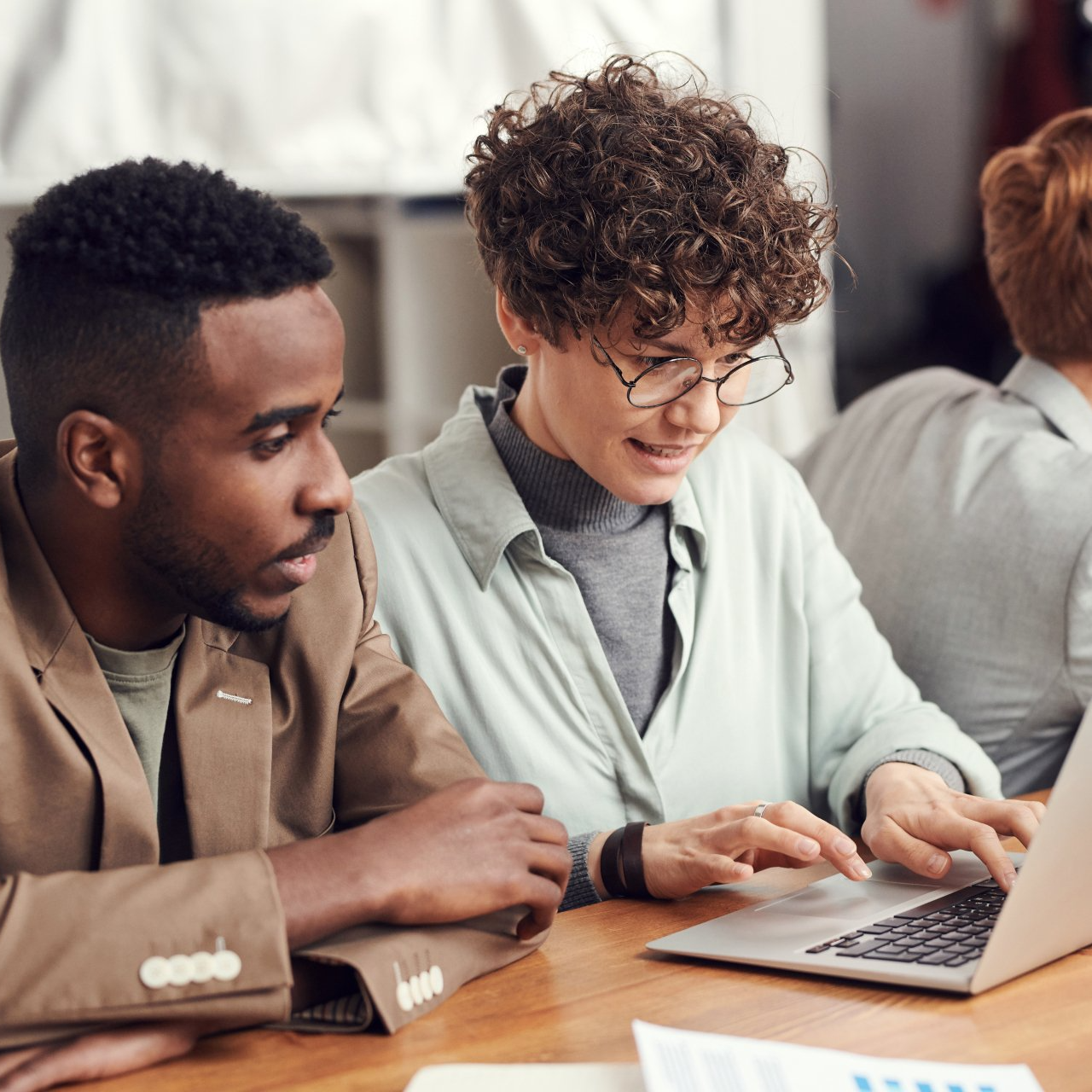 A man and a woman are sitting at a table looking at a laptop