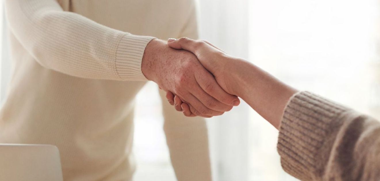 A man and a woman are shaking hands in front of a window.